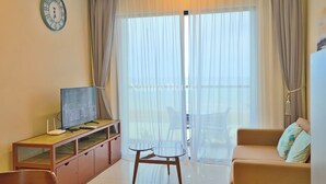 A living room with a TV, wooden cabinet, glass table, and beige sofa. - Timurbay Seafront Residences NatureHome (Kuantan)