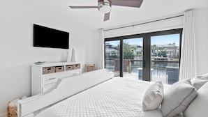 Een slaapkamer met een bed, een aan de muur bevestigde televisie, een plafondventilator en een balkon met uitzicht op de stad.