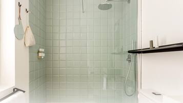 A modern bathroom with a glass shower enclosure, a white bathtub, and a shelf with toiletries.