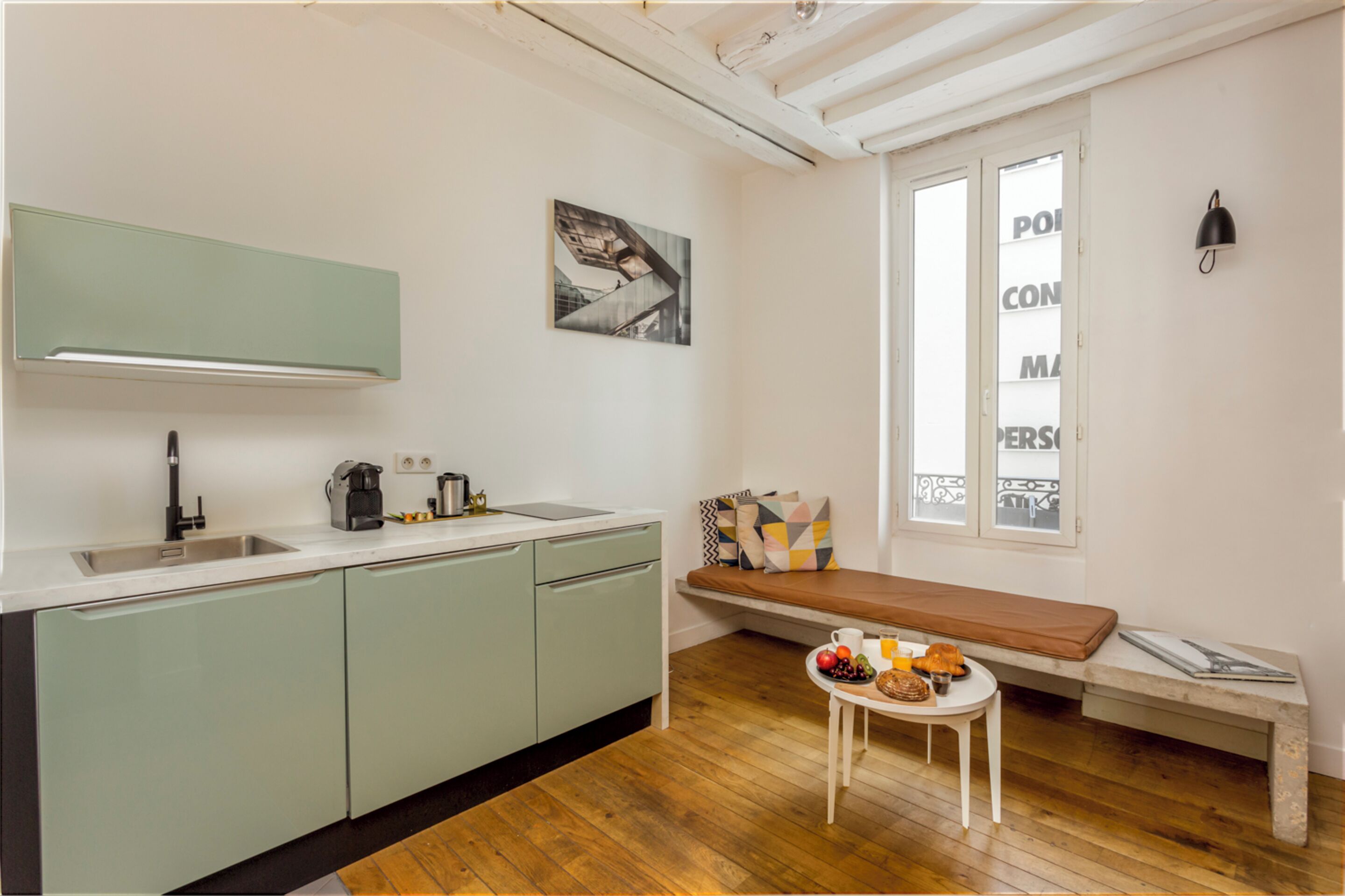 A compact kitchen with a sink, a coffee machine, and a bench with a table beside it.