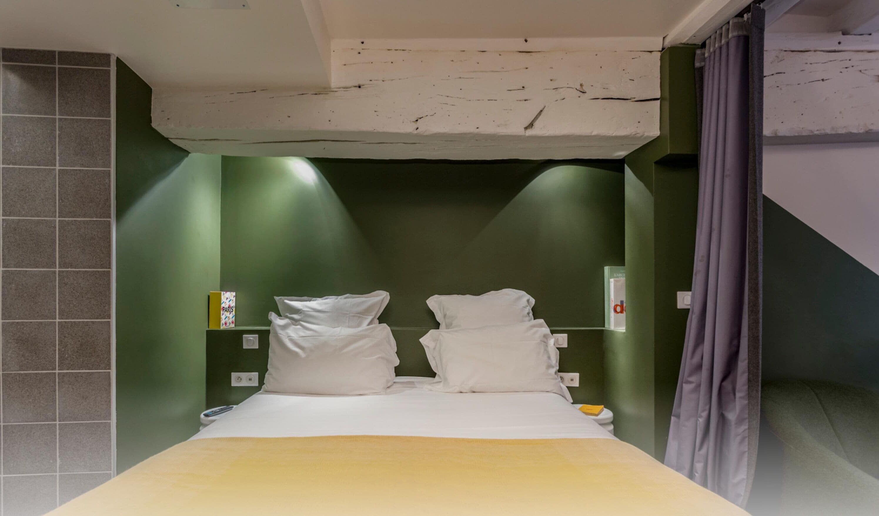Et lille, kompakt hotelværelse med en seng, et natbord og en grøn væg.