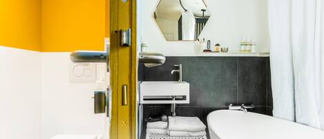 A modern bathroom with a white sink, dark tiled walls, a mirror, and a shower area.