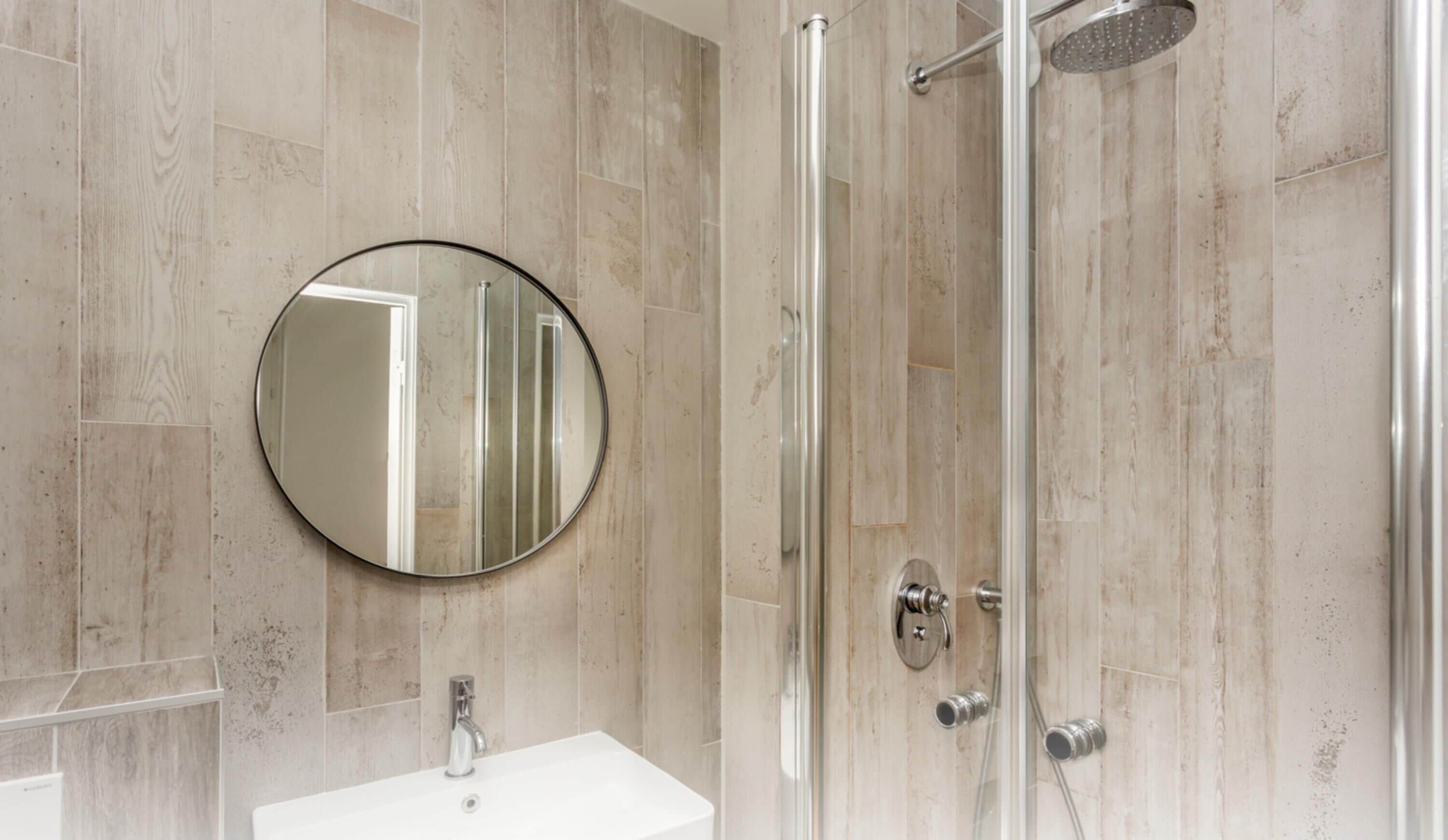 A bathroom with a round mirror, a sink, and a glass-enclosed shower.