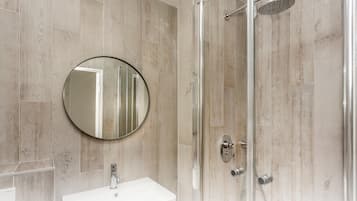 A bathroom with a round mirror, a sink, and a glass-enclosed shower.