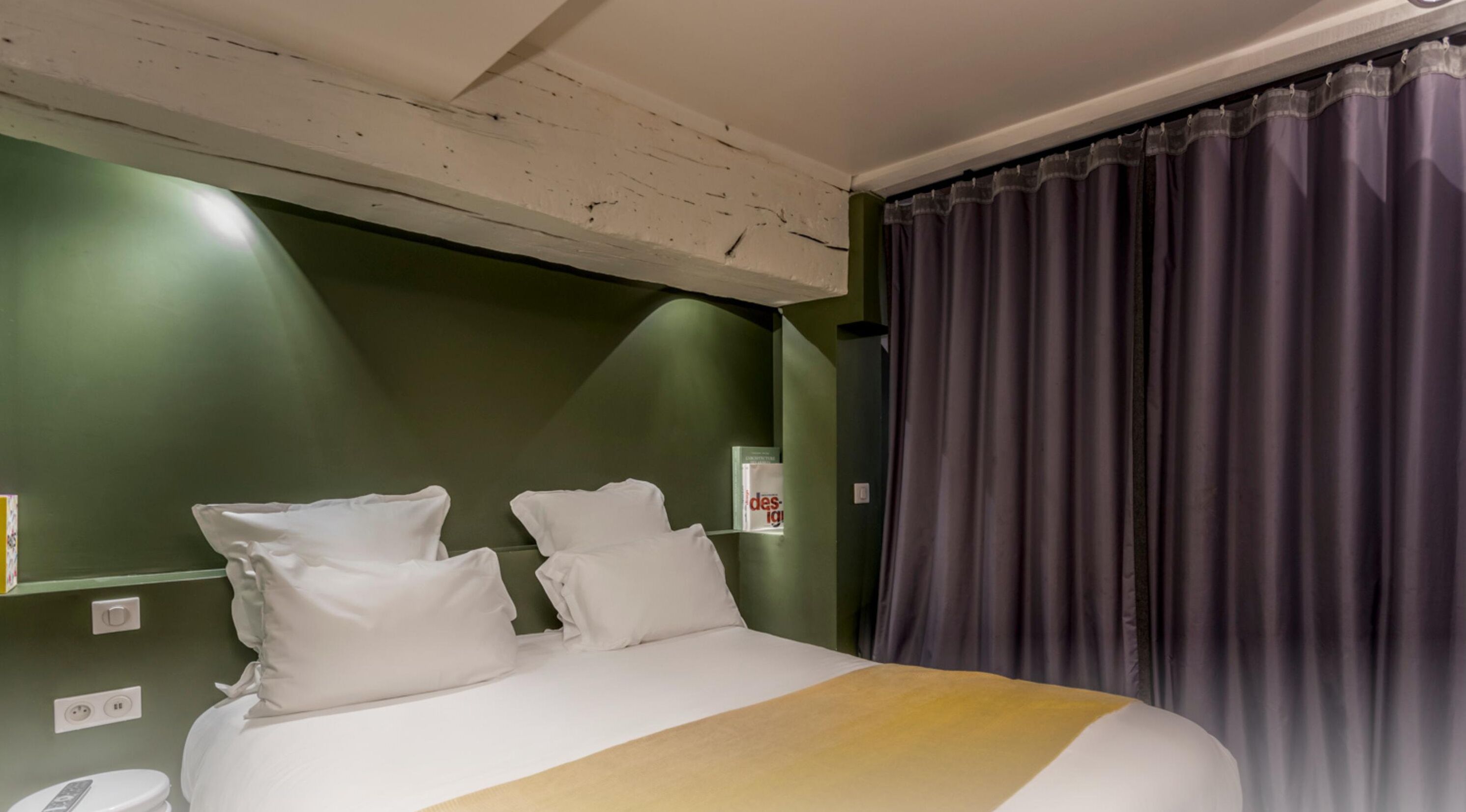Hotelkamer met een bed, twee kussens, een nachtkastje, een telefoon en een gordijn.