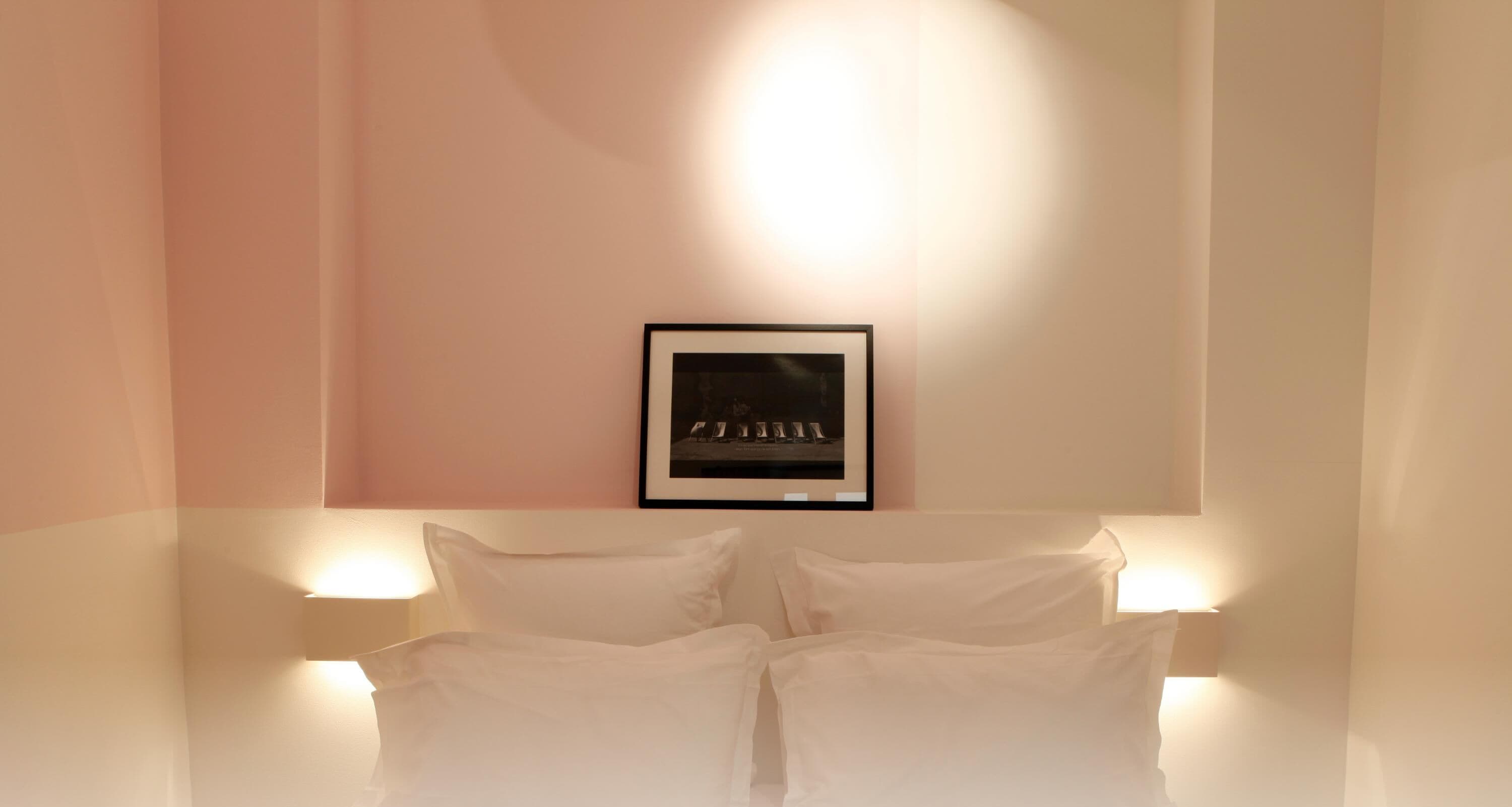 A hotel room with a bed centered in the frame, flanked by two wall-mounted lamps.