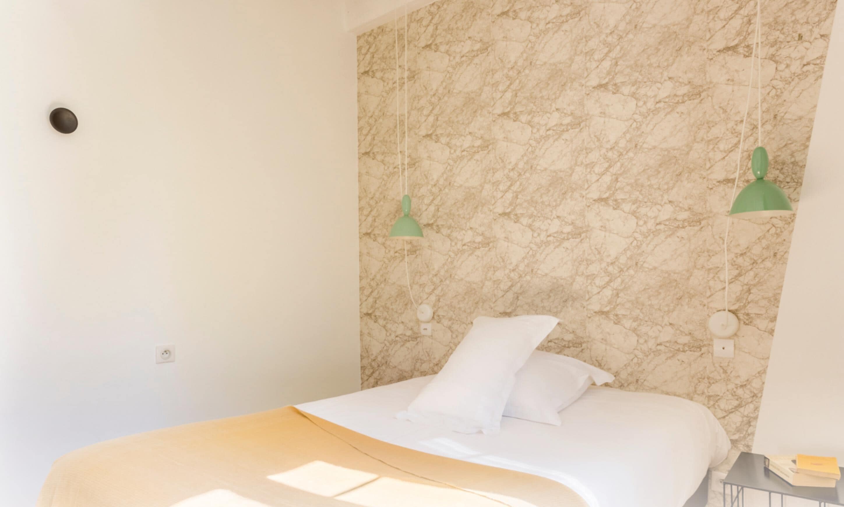 A bedroom with a bed, a marble wall, and two hanging green lamps.