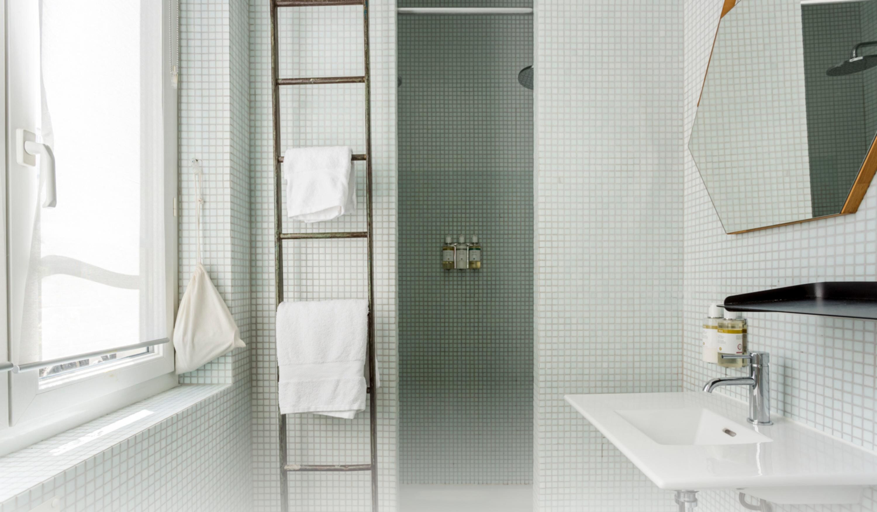 A bathroom with a white sink, a mirror, and a shower area with a ladder.