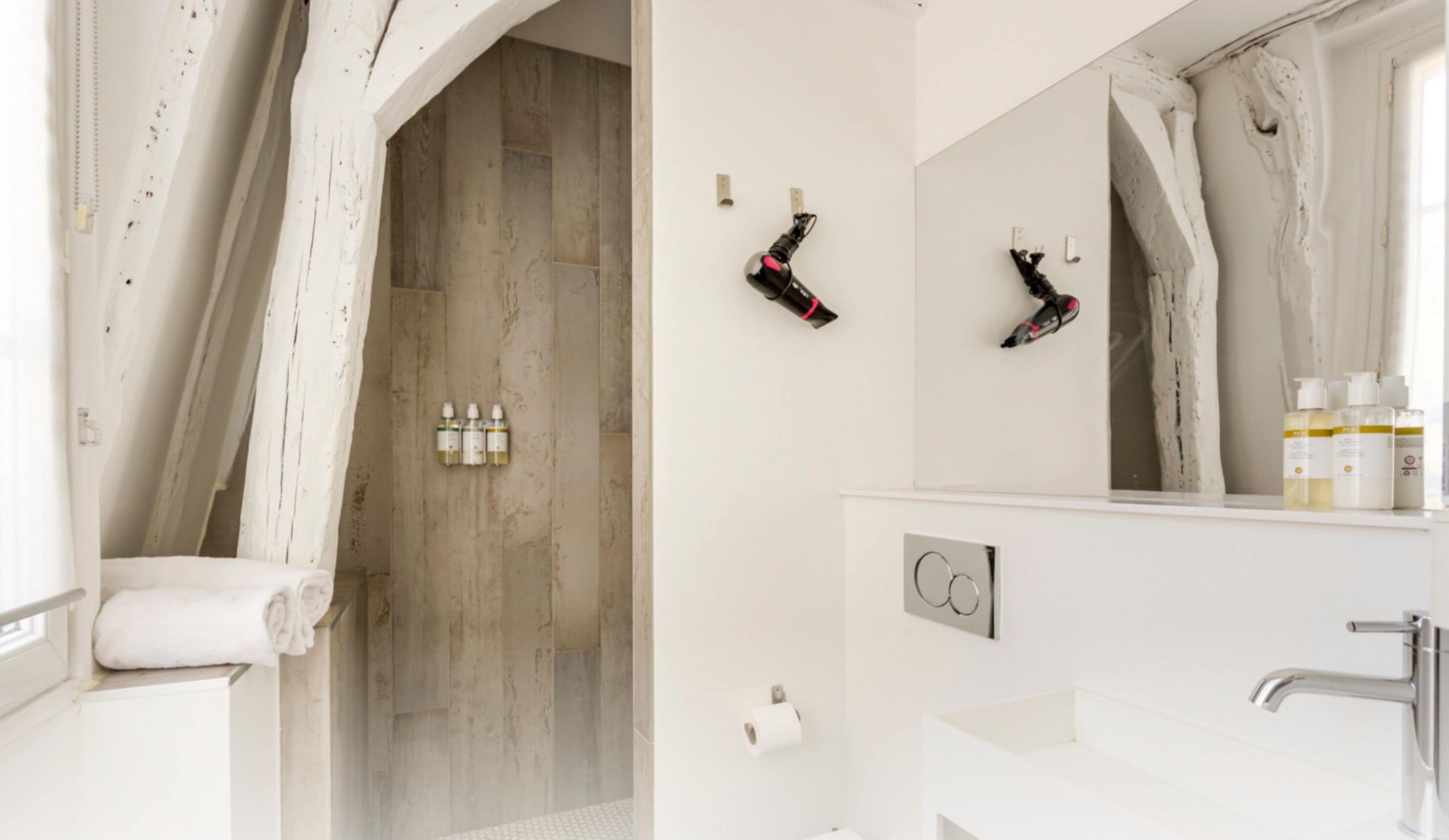 Une salle de bain moderne équipée d’une douche, d’un porte-serviettes, d’un miroir et de produits de toilette posés sur le comptoir.