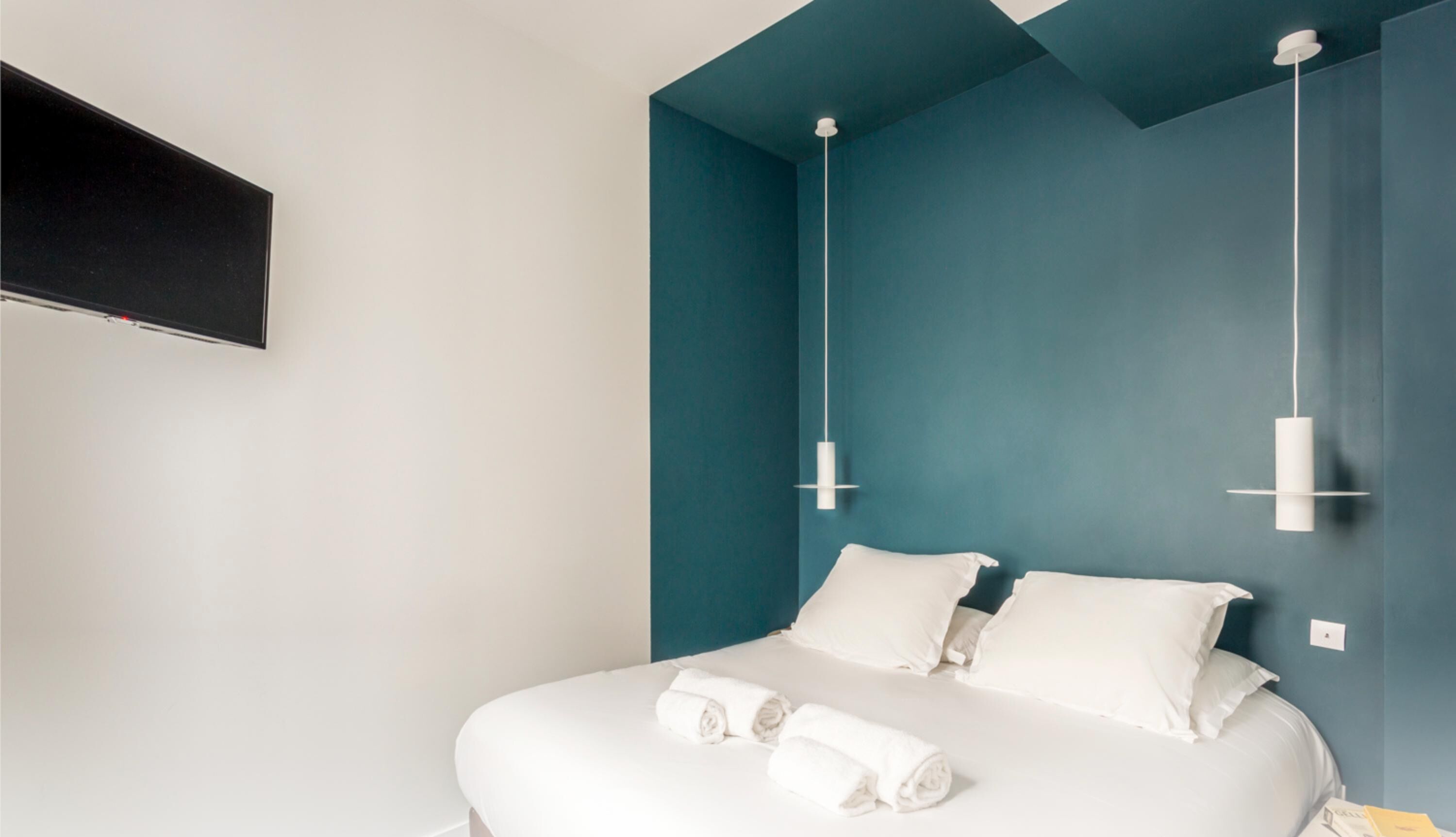 Ein modernes Hotelzimmer mit einem Bett, weißen Leinen und einem an der Wand befestigten Flachbildfernseher.