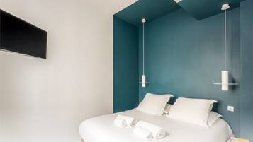Ein modernes Hotelzimmer mit einem Bett, weißen Leinen und einem an der Wand befestigten Flachbildfernseher.