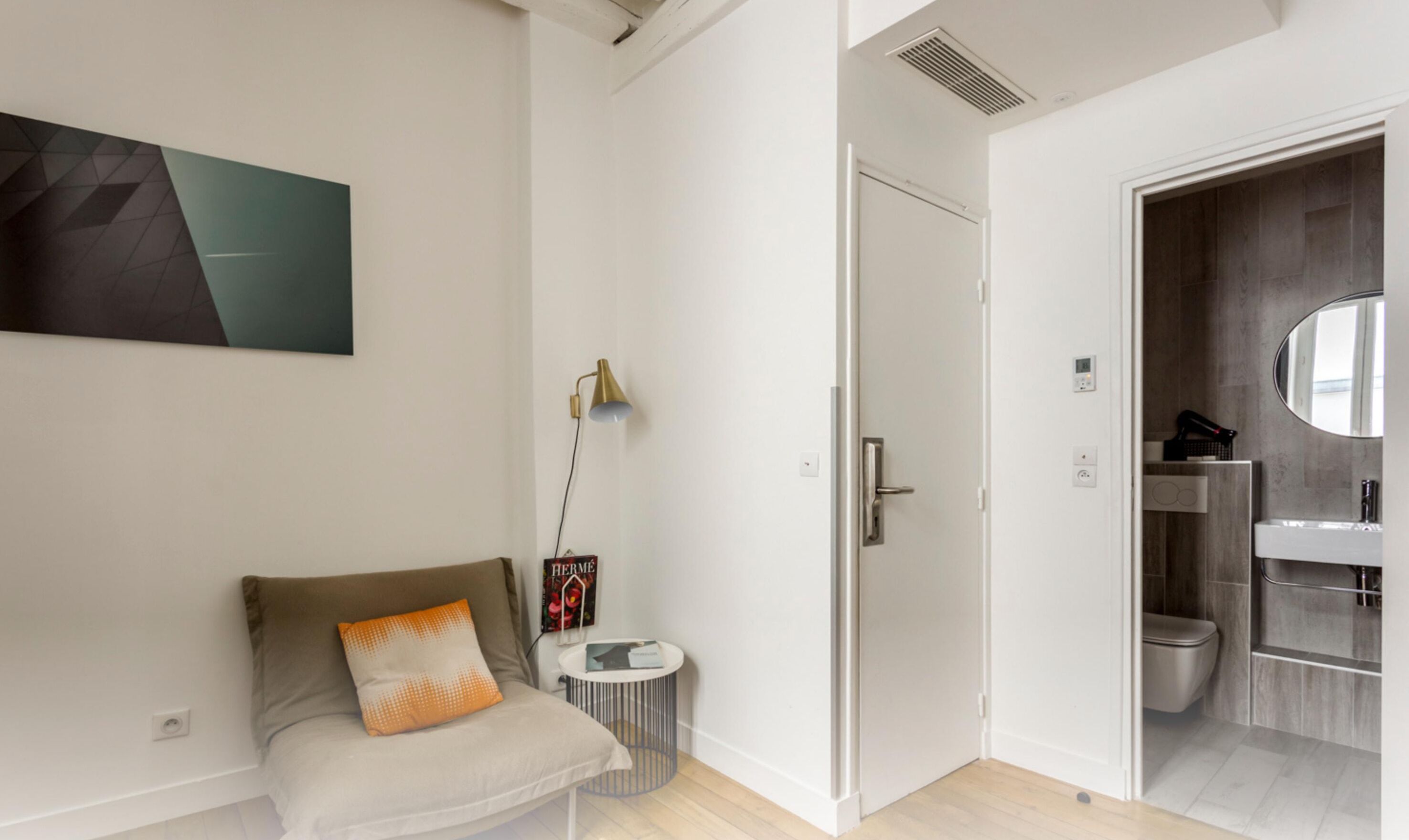 Een moderne kamer met een bank, een klein bijzettafeltje, een deur naar een badkamer en een kunstwerk aan de muur.