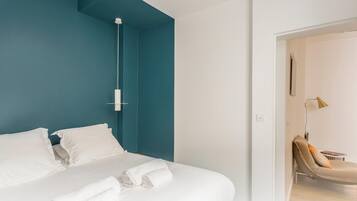 A modern hotel room with a teal accent wall, a bed with white linens, and a single roll of white towels.