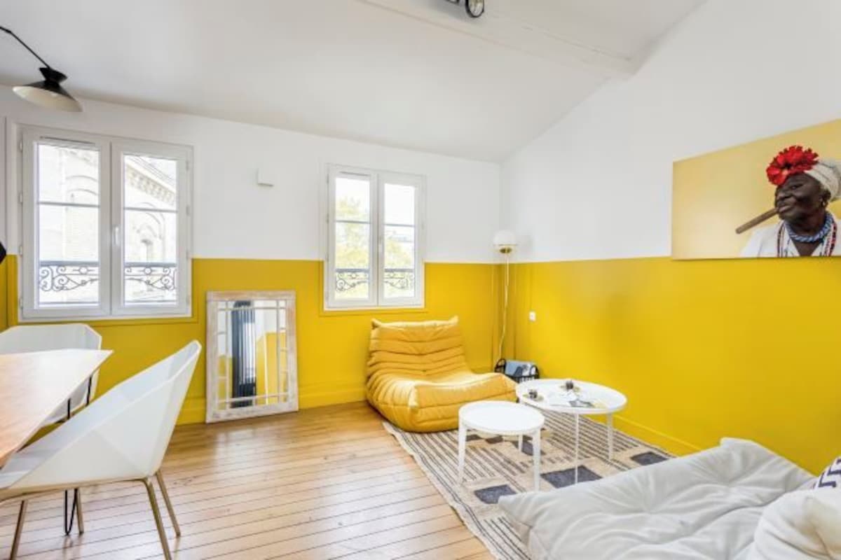 A room with a yellow and white color scheme, featuring a sofa, a small round table, and a bed.