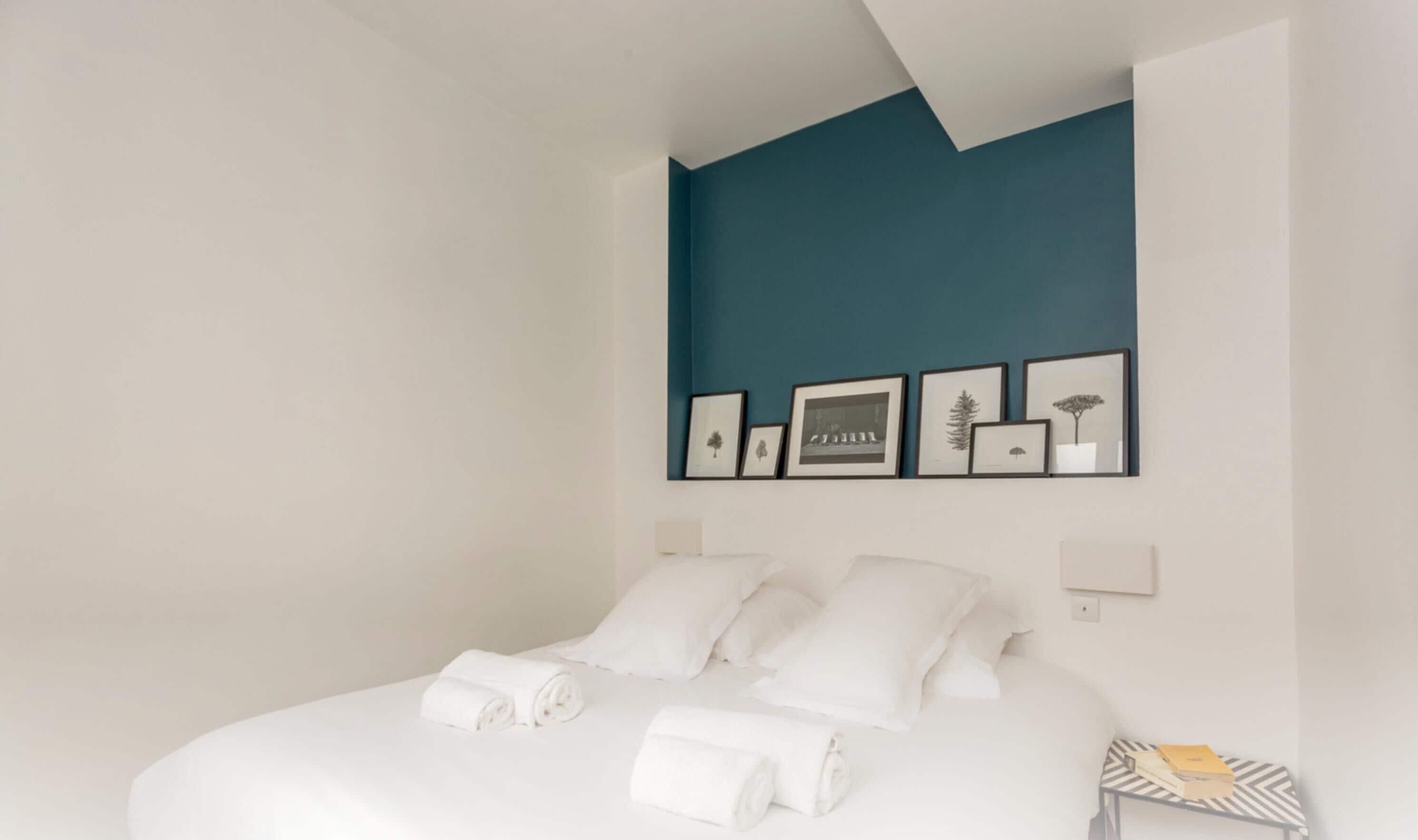 A hotel room with a bed, white linens, and a teal accent wall.