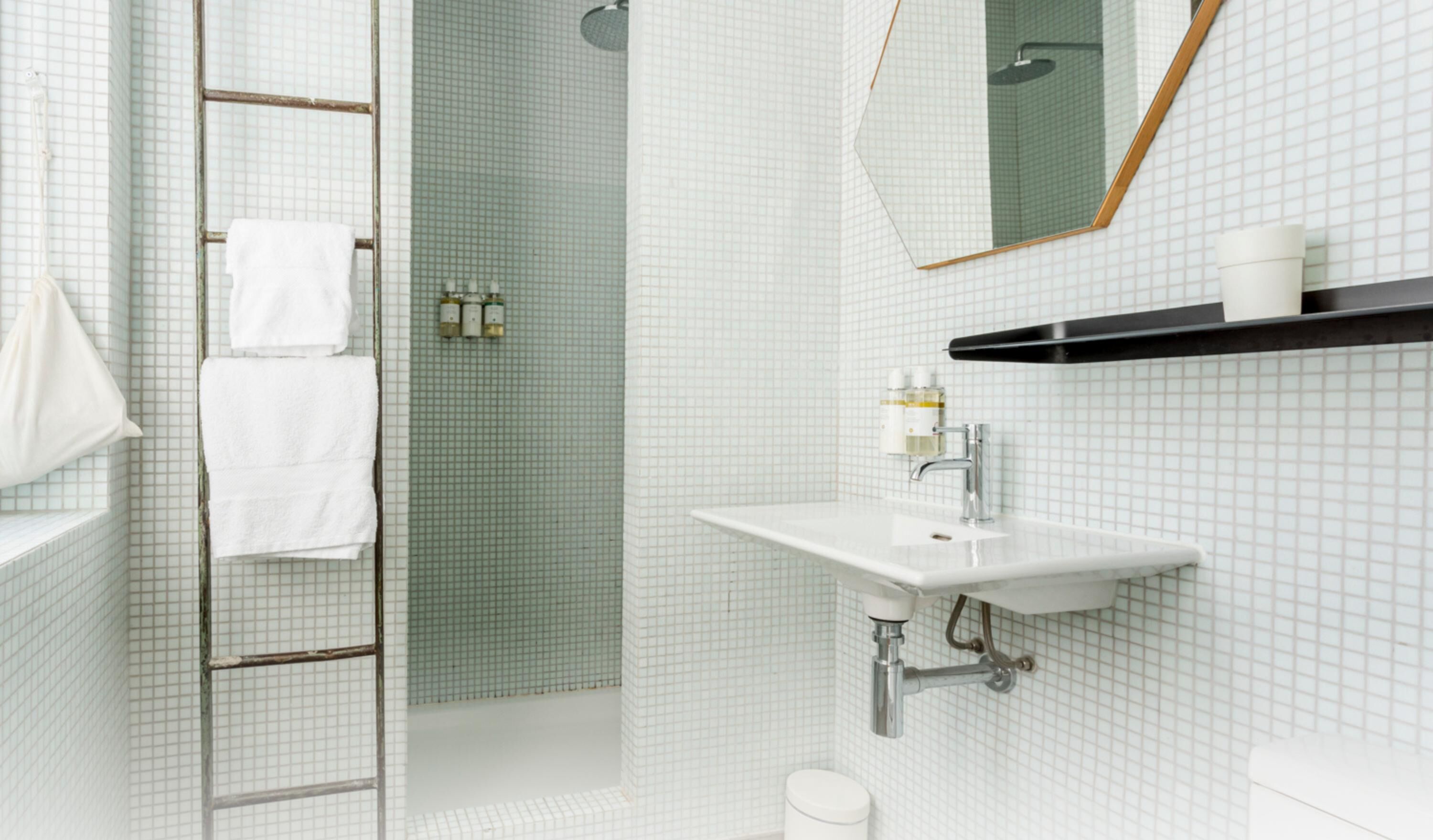 A bathroom with a shower, a sink, and a mirror. There are towels hanging on a rack and toiletries on the wall.