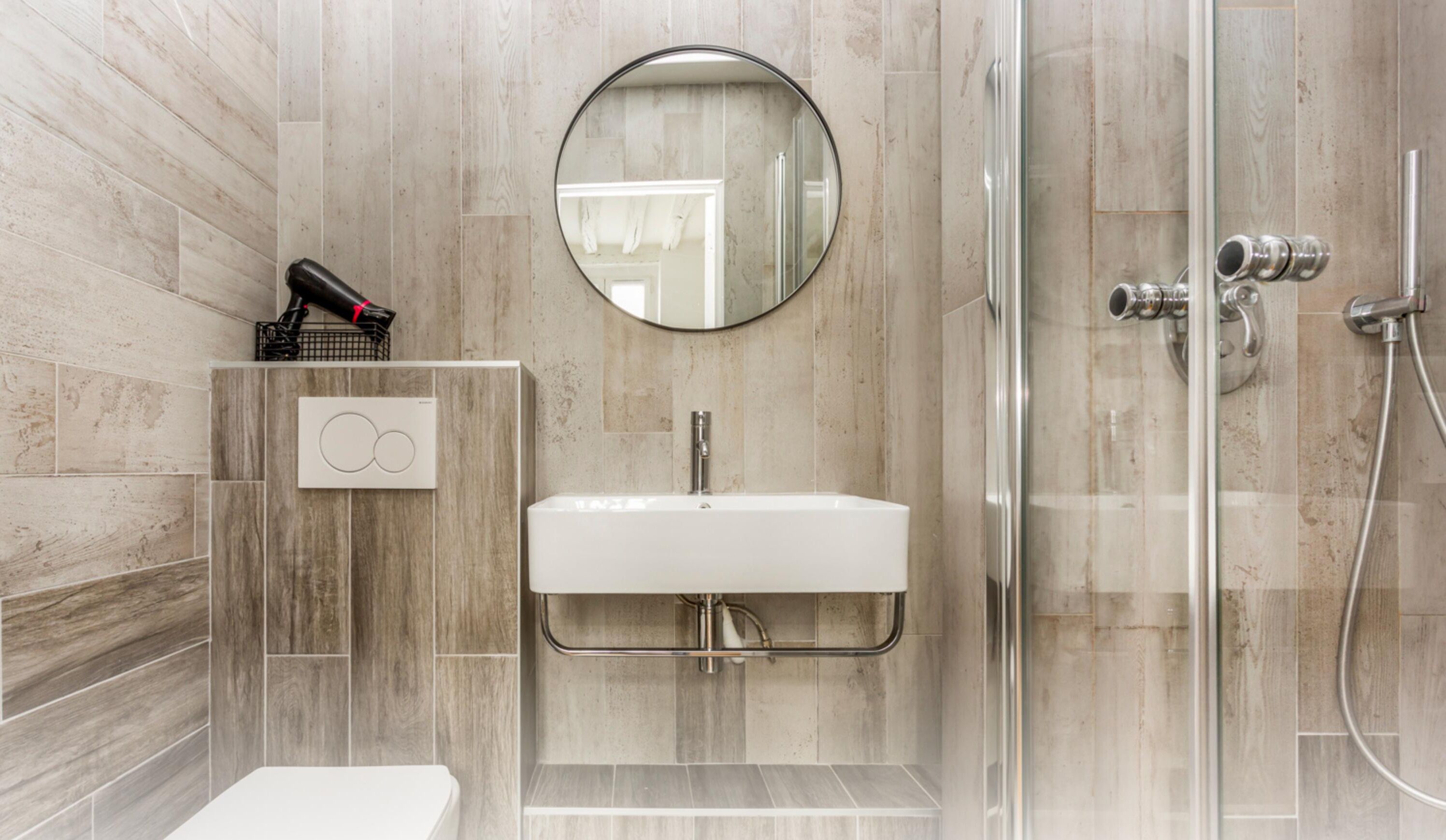 A modern bathroom with a white sink, a round mirror, and a glass shower enclosure.
