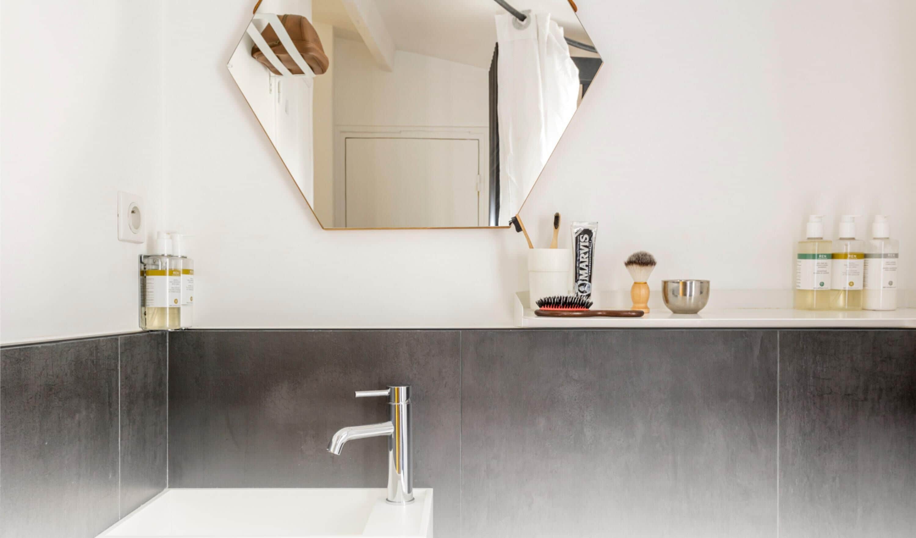 Une salle de bain moderne avec un grand miroir, un lavabo et des articles de toilette disposés sur le comptoir.