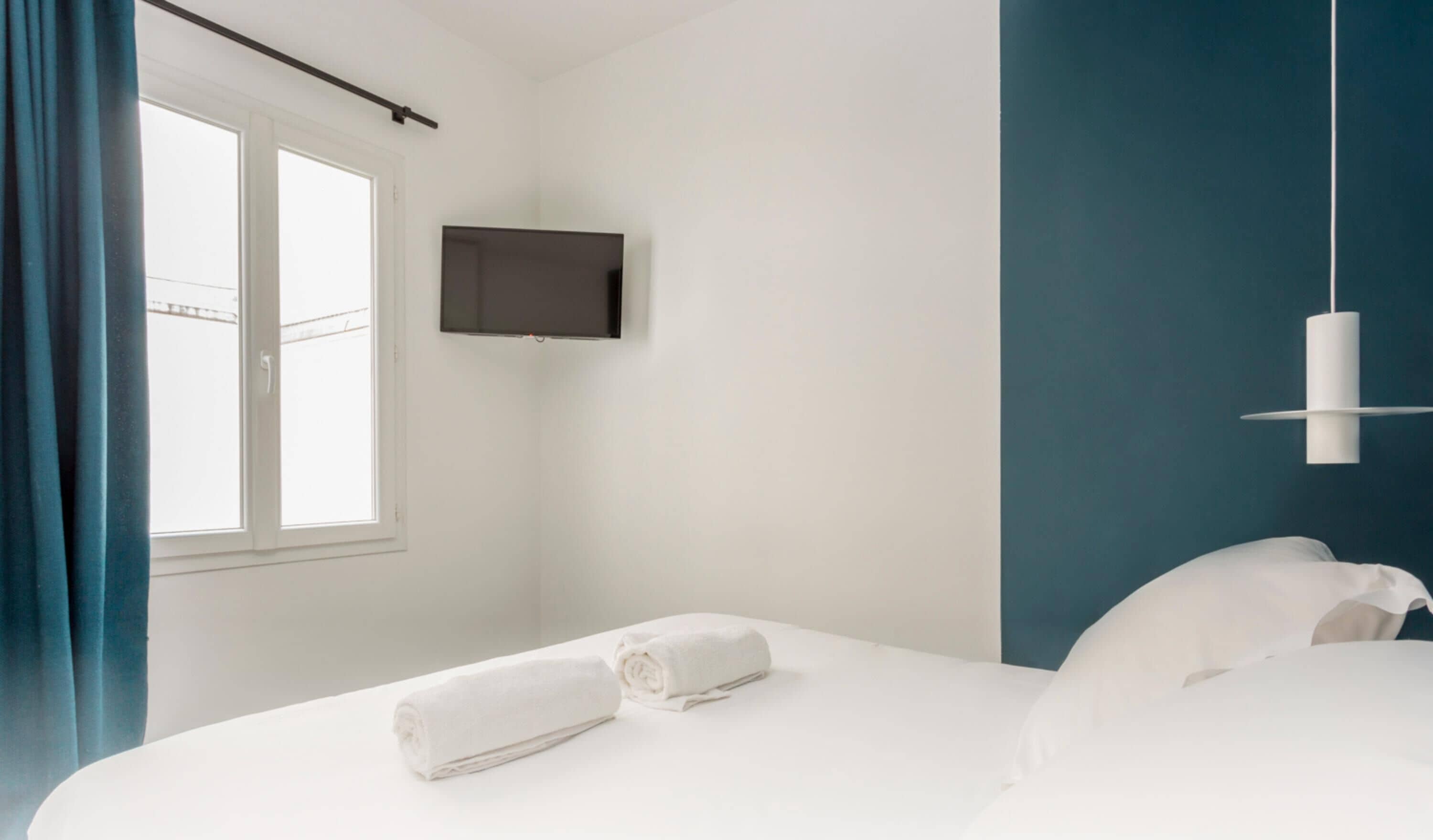 A hotel room with a bed, a TV mounted on the wall, and a window with curtains.