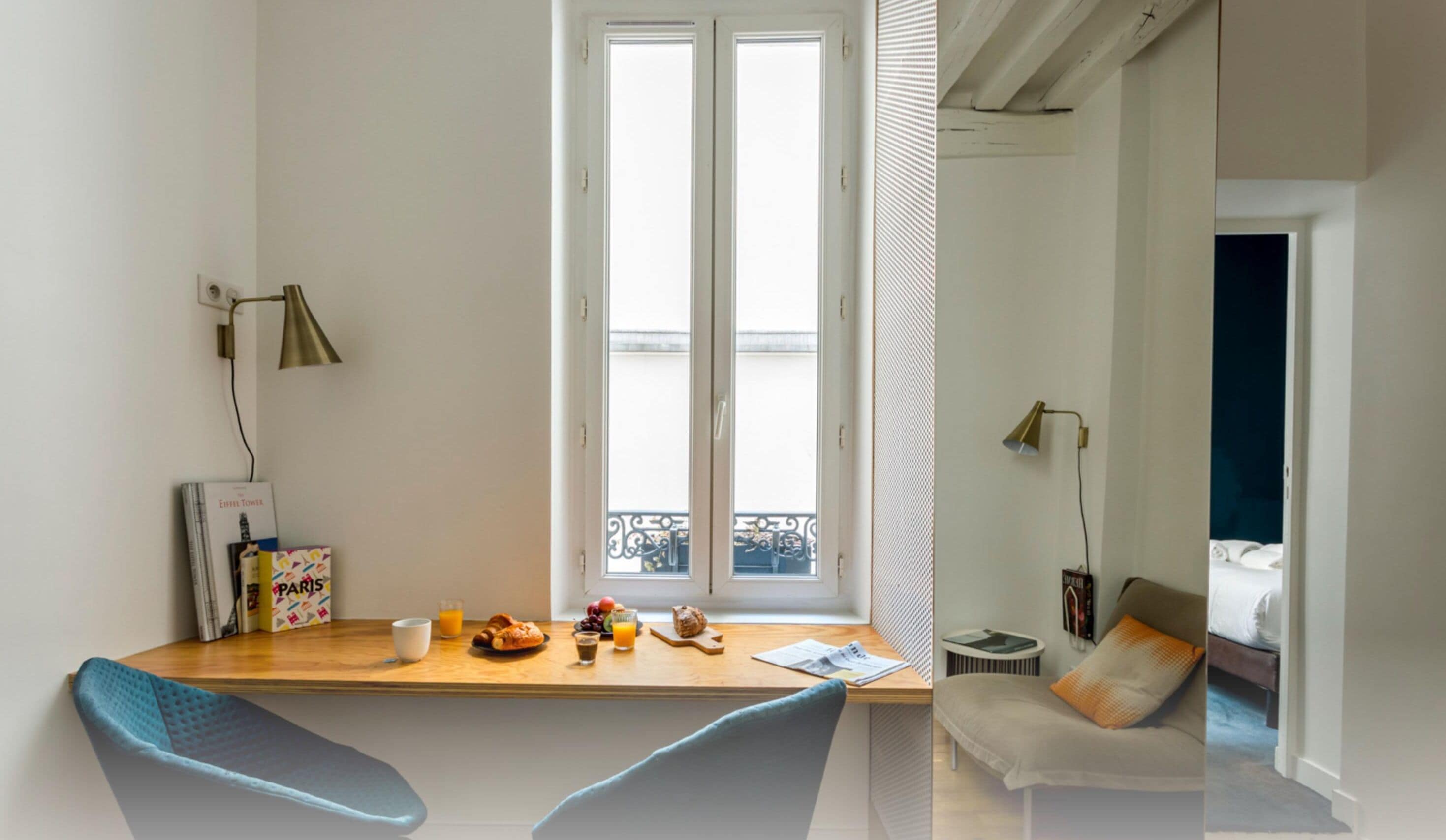 A modern room with a wooden desk, a chair, a bed, and a window with a view of a balcony.