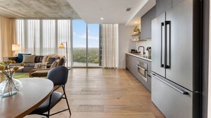 A modern kitchen with a large refrigerator, wooden flooring, and a view of a cityscape through large windows. - Sunshine Condo in Downtown Austin (Austin)