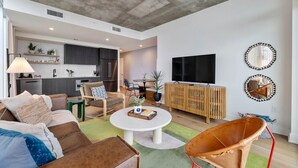 A modern living room with a sofa, coffee table, and a TV. There is a kitchen area with cabinets and a dining table. - Sunshine Condo in Downtown Austin (Austin)