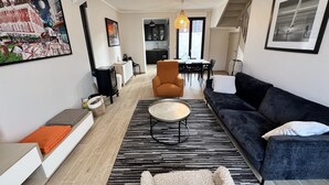 A modern living room with a sofa, armchair, coffee table, and a dining area in the background.