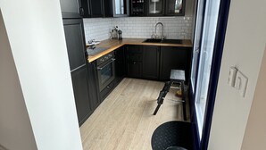A modern kitchen with black cabinets, a wooden countertop, a black trash bin, and a hanging pendant light.