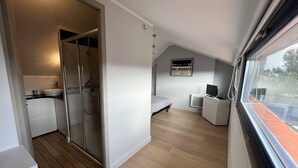 A compact bedroom with a shower, a bed, a TV, and a small desk.
