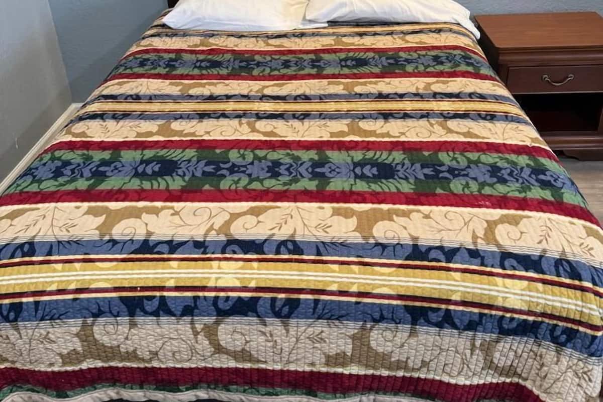 A bed with a patterned bedspread, a wooden headboard, and a nightstand with a drawer.