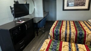 A hotel room with a desk, a television, a framed picture on the wall, and two beds with patterned bedding. - Midtown Lodge (Jacksonville)