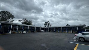 A large parking lot with multiple cars and a building with blue and white exterior. - Midtown Lodge (Jacksonville)