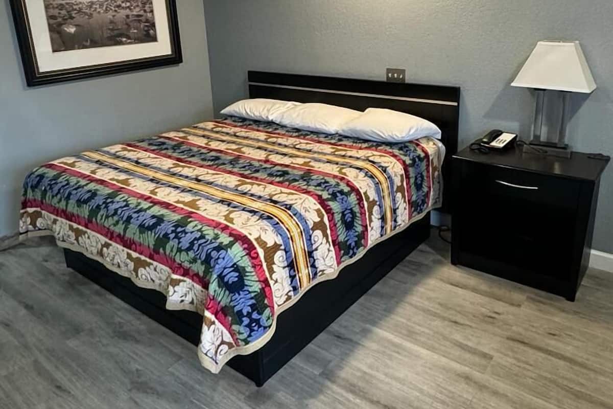 A bedroom with a bed, a nightstand, a lamp, and a framed picture on the wall.