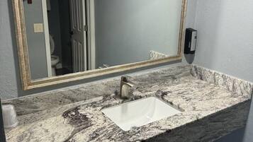 Une salle de bain avec un lavabo en marbre, un grand miroir avec un cadre doré et un sèche-mains fixé au mur.