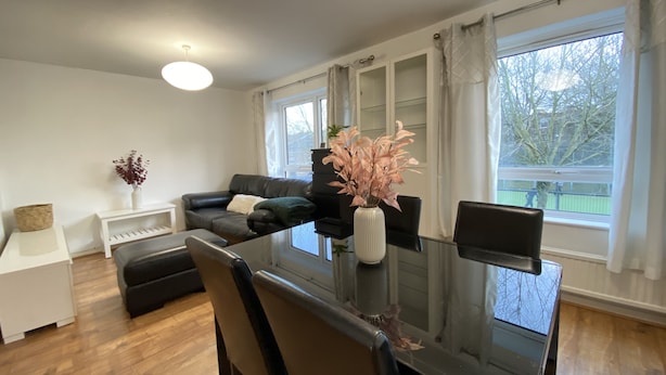 Un salon moderne avec une table à manger en verre, un canapé en cuir noir et une console blanche ornée d’un vase.