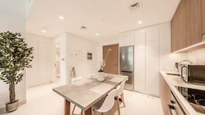 A modern kitchen with a dining table, white chairs, a potted plant, and a built-in microwave. - Tanin - Exquisite 1BR Apartment with Sea View  (Dubai)