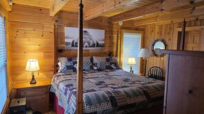 Quarto de cabana de madeira com cama de dossel, duas luminárias de cabeceira, cômoda de madeira e uma grande moldura na parede.