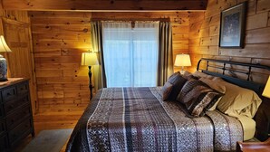 Een slaapkamer in een houten hutje, met een bed, twee bedlampen, een dressoir en een lijst aan de muur.
