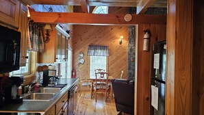 A cozy cabin interior with wooden walls, a kitchen area with a stove, sink, and refrigerator, and a dining area with a table and chairs. - Magnolia-Cabin sits on Coosa creek with a breath taking view of the falls (Blairsville)