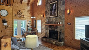 A cozy cabin interior with wooden walls, a stone fireplace, a dining area, and a living room with a sofa and lamp. - *FAMILY GETAWAY*Deck/Firepit/HOT TUB & Fireplace (Blairsville)