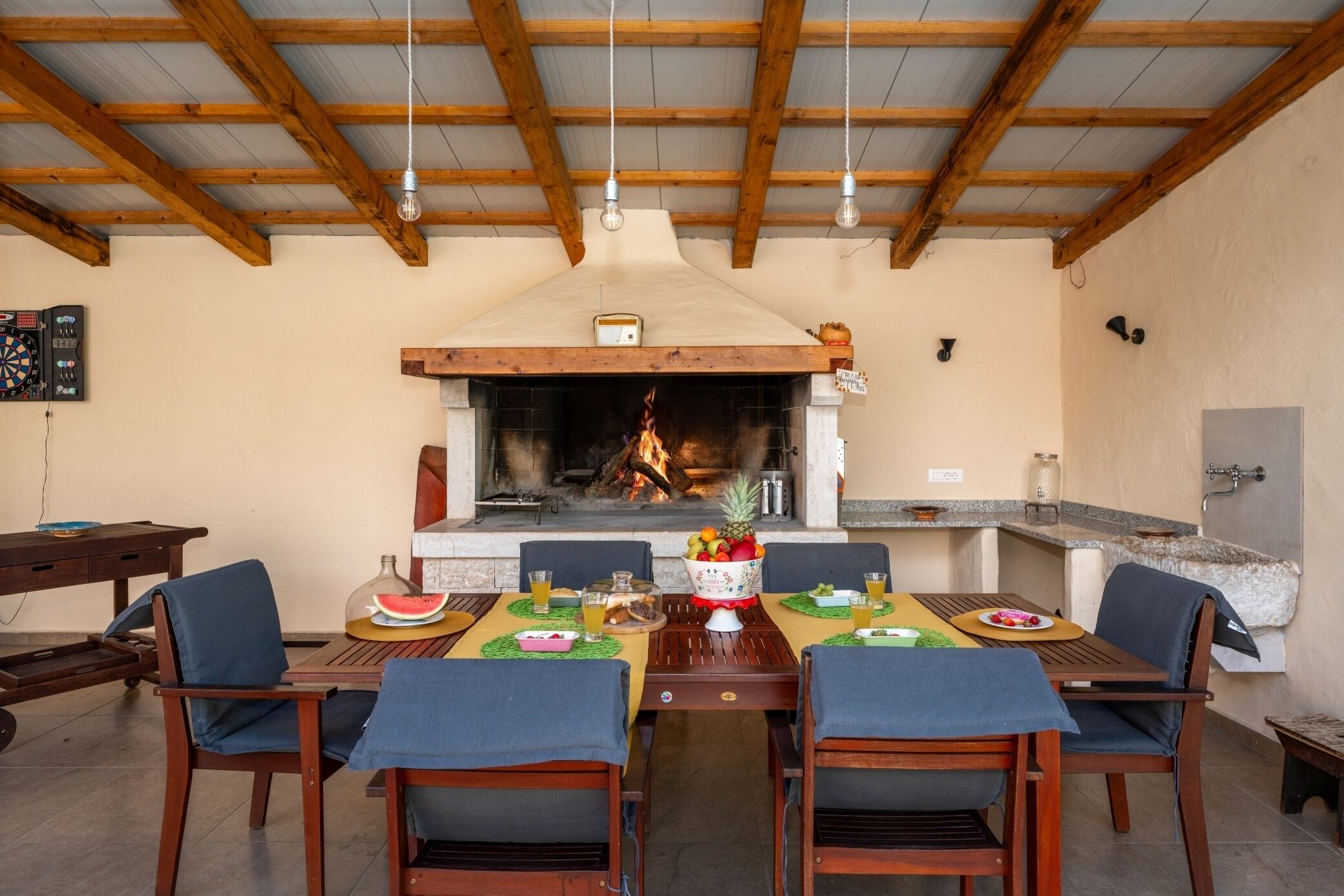 A dining area with a wooden table set for four, surrounded by chairs, a fireplace, and a stone countertop.