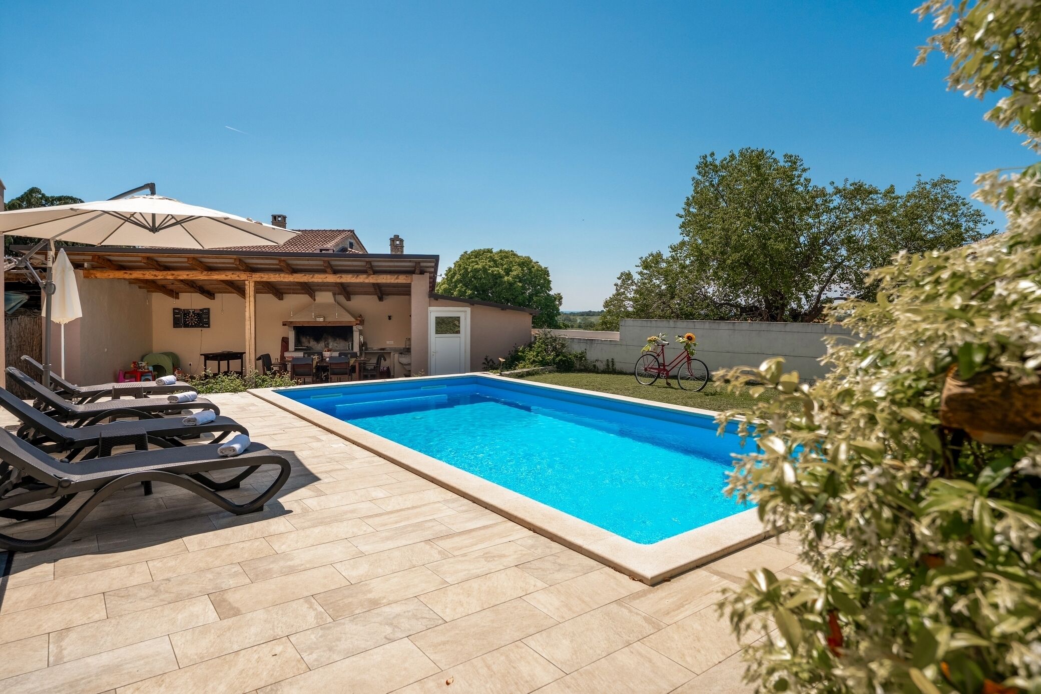 A swimming pool with lounge chairs, a covered patio, and a bicycle in the background.