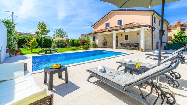 Ein Schwimmbecken mit Liegestühlen und einer überdachten Terrassenanlage.
