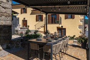 An outdoor dining area with a stone table and wicker chairs, surrounded by potted plants and a stone wall.