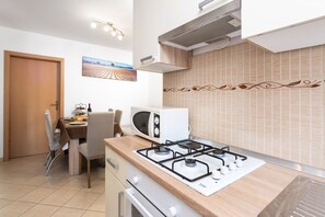 Compact kitchen with gas stove, microwave, and dining table for two, set amidst a modern design with decorative tiles and artwork.