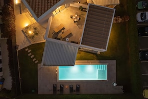 Vista aérea de uma área externa moderna com piscina, área de refeições com mesas e cadeiras, e uma área de estar coberta.