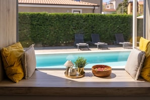 A window seat with a view of a swimming pool, lounge chairs, and a wooden bowl with flowers.