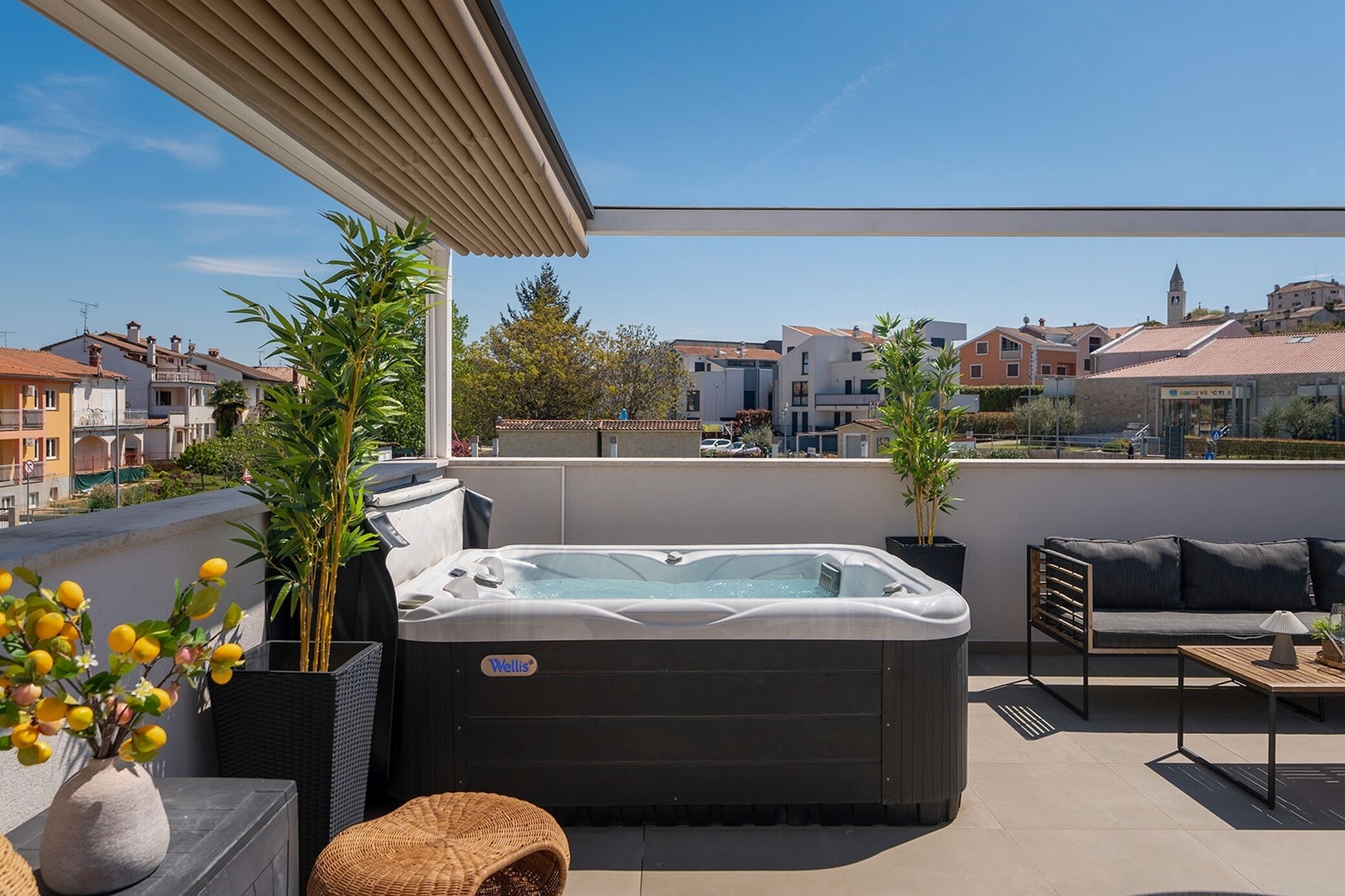 A rooftop terrace with a hot tub, outdoor furniture, potted plants, and a view of the cityscape.