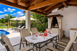 An outdoor patio with a pool, a table set for dining, and a stone fireplace.