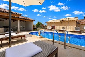 Un espace aménagé au bord de la piscine, avec des chaises longues, des parasols et une piscine.